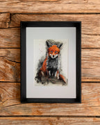 Another version of the watercolour fox painting in a frame on an wooden surface.