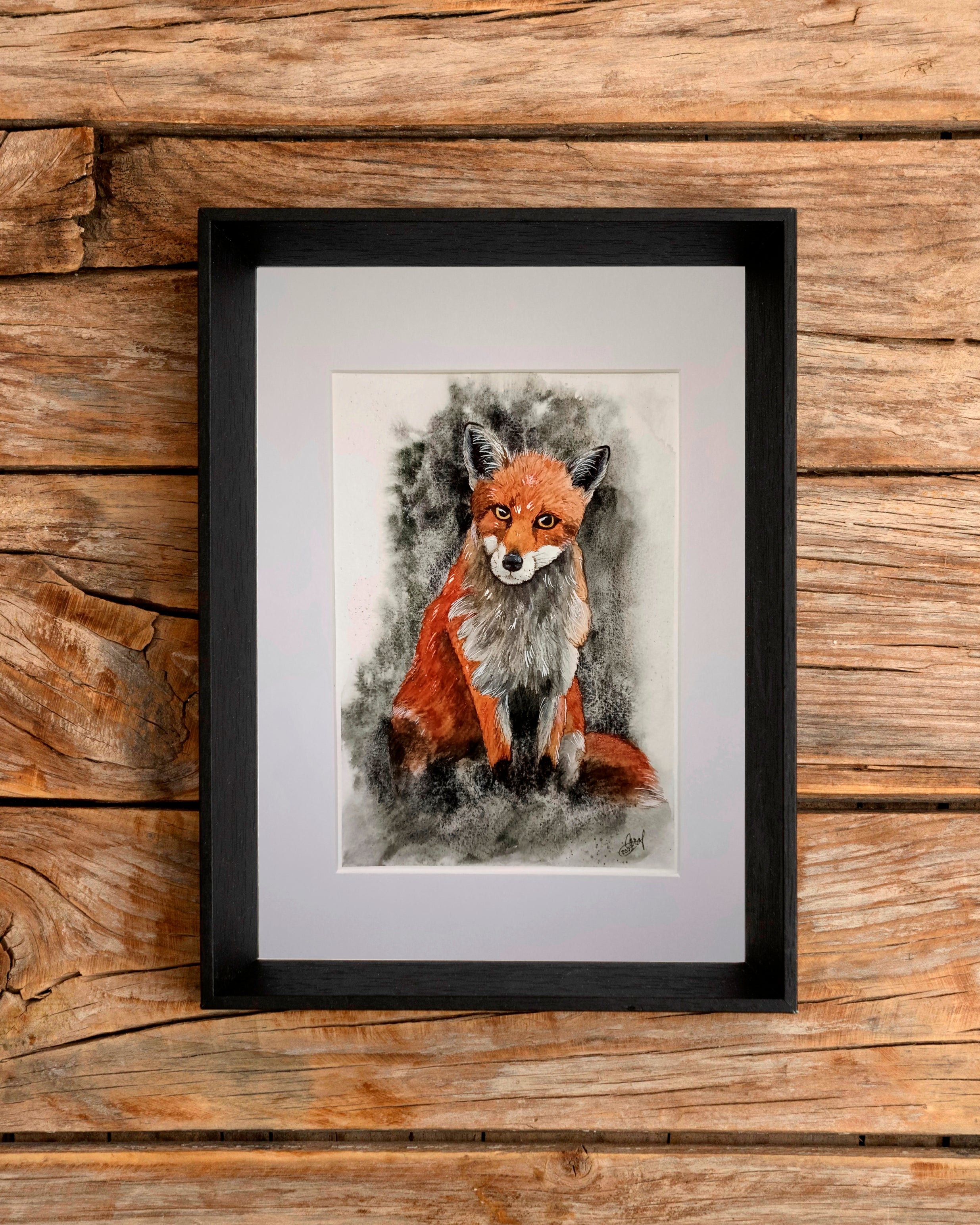 Framed artwork of an original watercolour fox painting on a wooden surface.