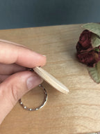 Hand holding a wooden keychain sideways to show the thickness and look of the keyring edge.