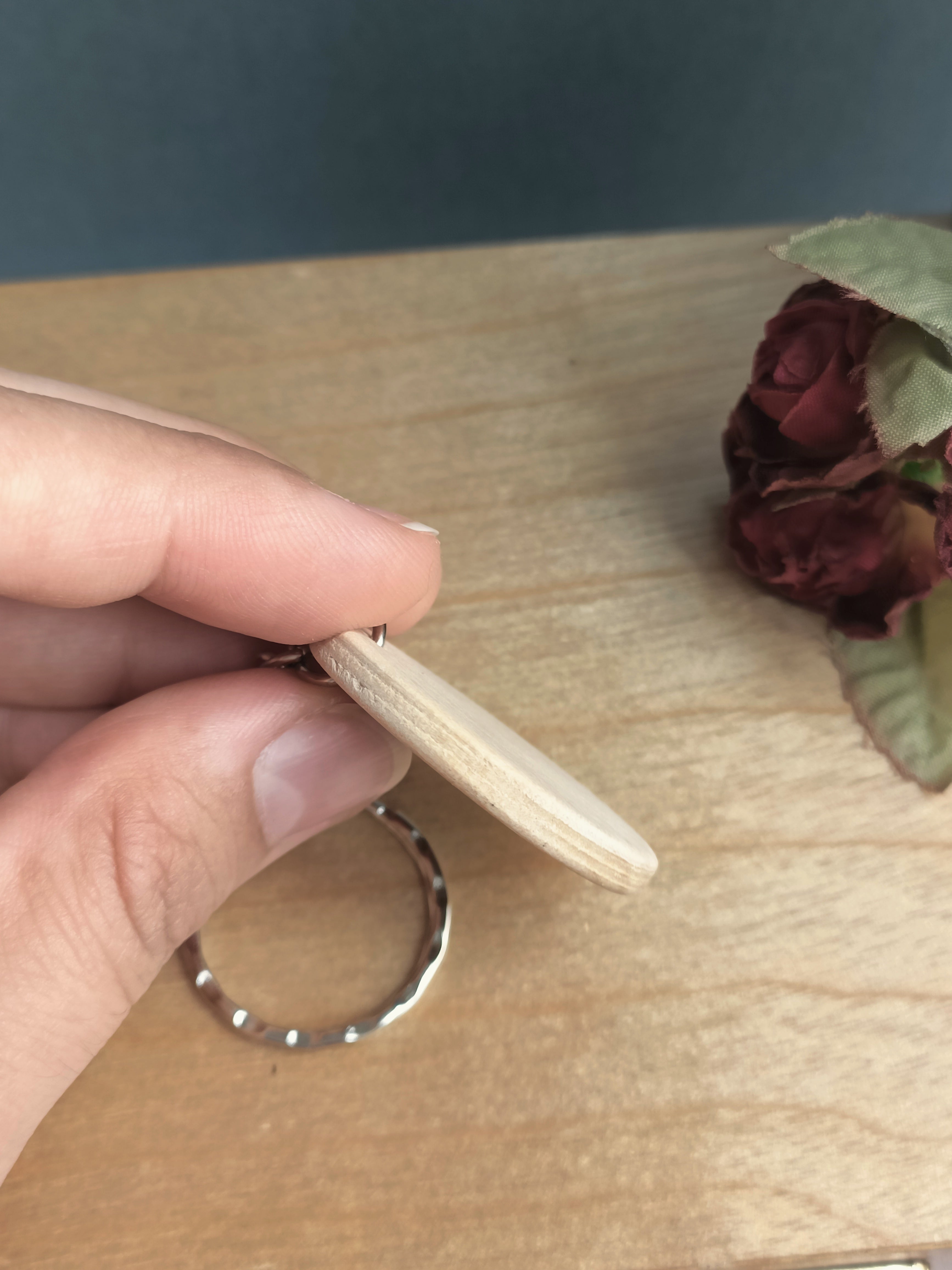 Hand holding a wooden keychain sideways to show the thickness and look of the keyring edge.