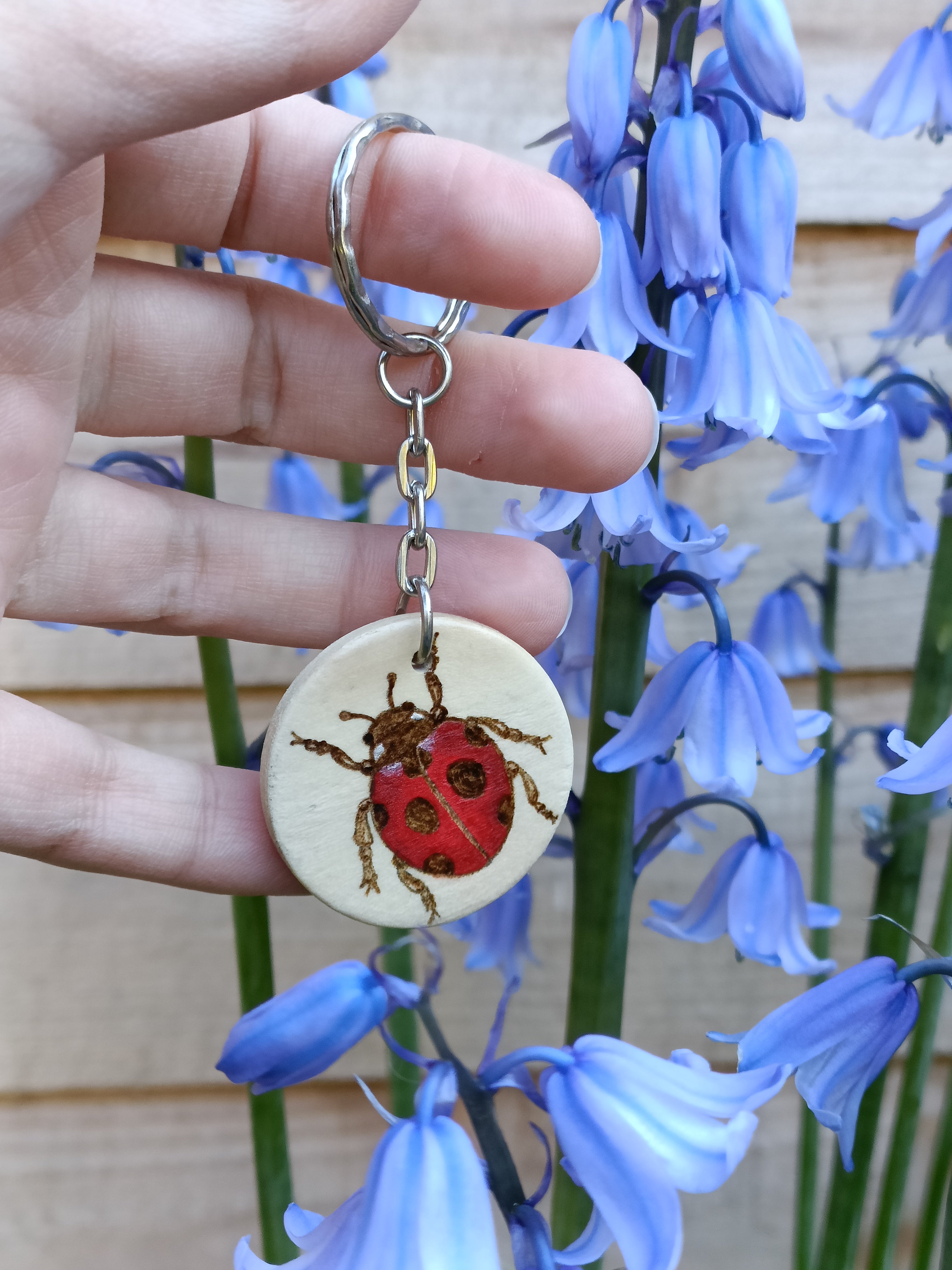 Hand holding a circle ladybird keychain, woodburned and painted by hand. Shown outside in natural light.
