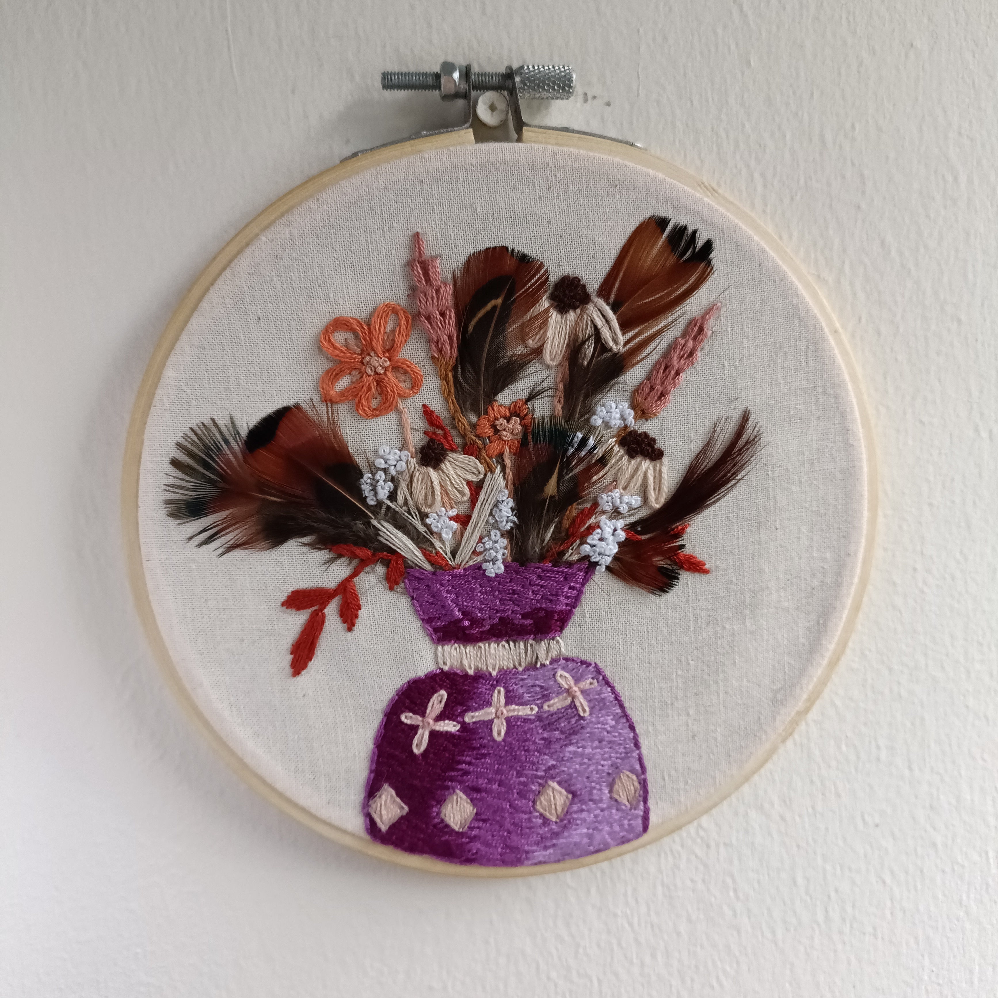Embroidery hoop with floral and feather design on a white background