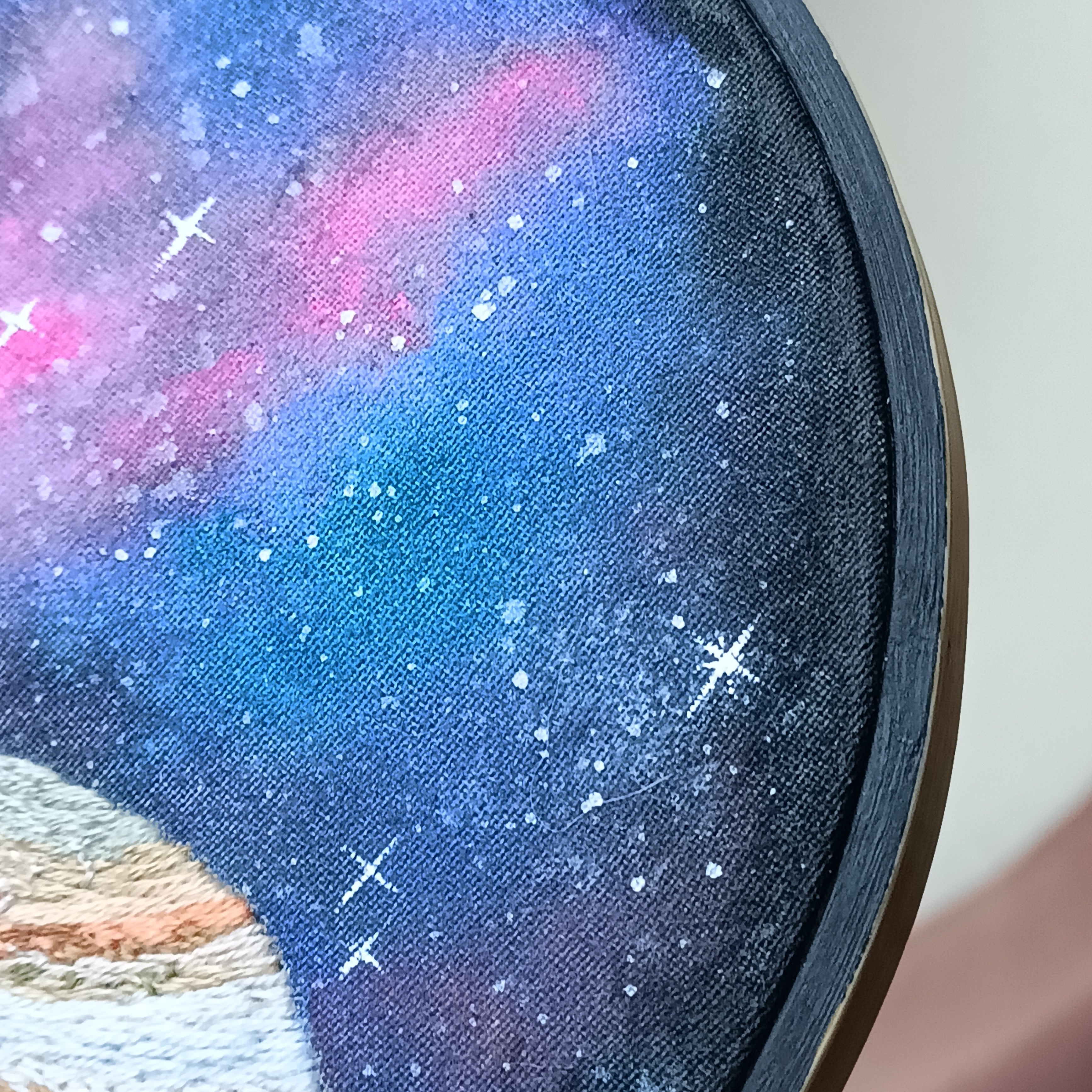 Close-up of embroidery hoop with galaxy-themed fabric design featuring stars and planets.