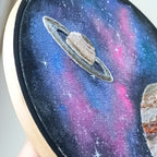 Embroidery hoop with a space-themed design featuring Saturn and stars.