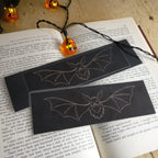 Closer shot of two black bat-themed bookmarks on an open book with pumpkin lights.