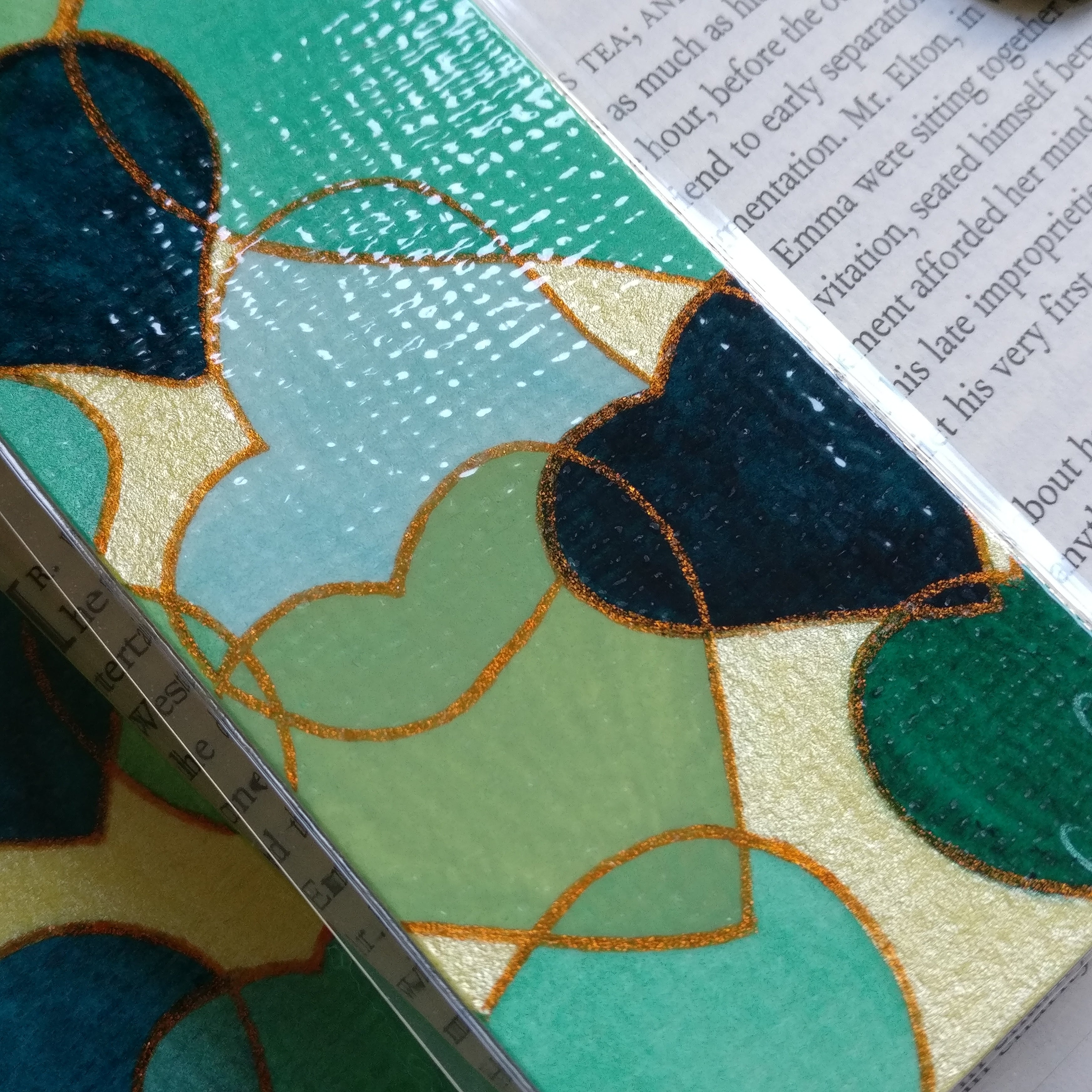 Close-up of a green watercolour hearts bookmarks with glitter orange outlines.