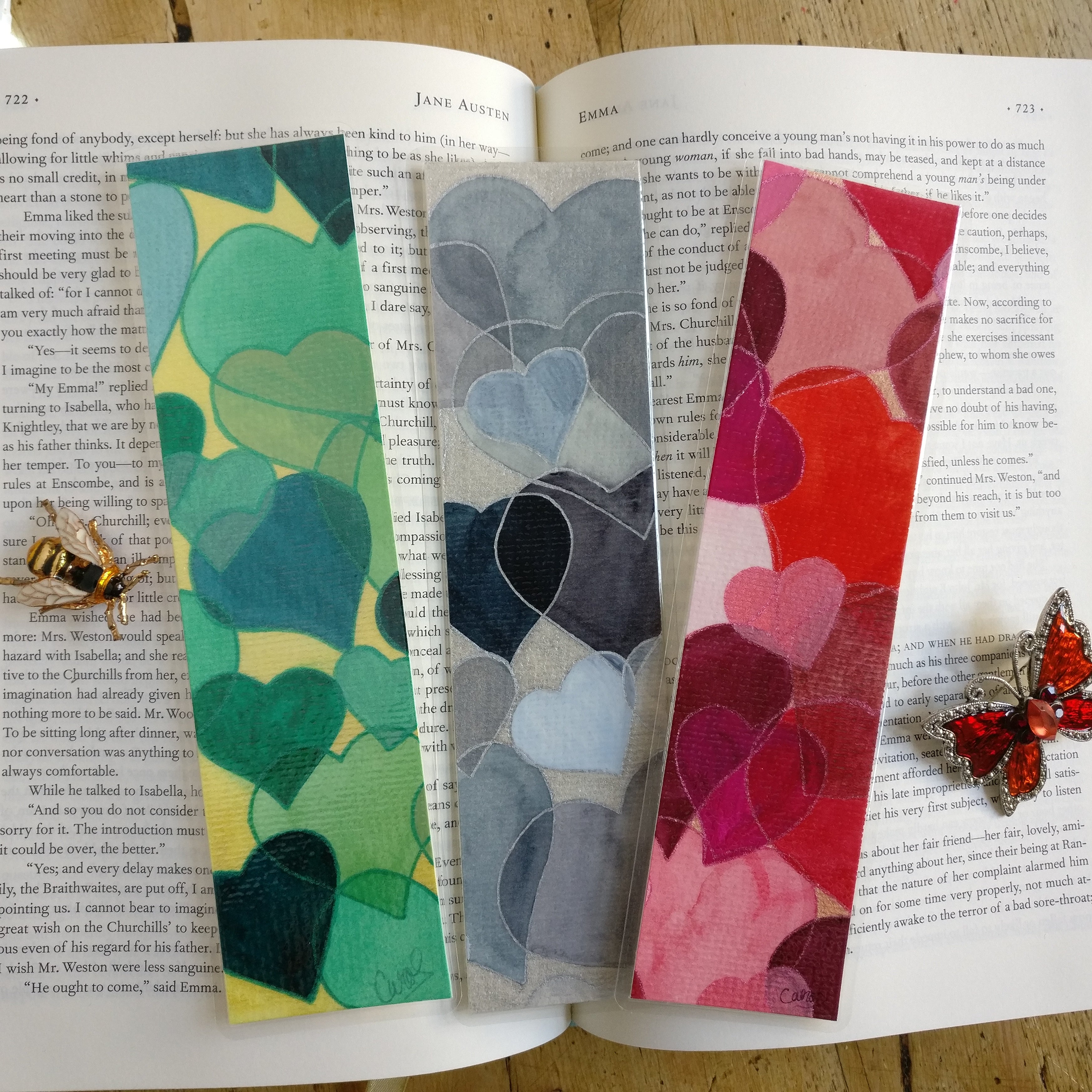 Colorful hand-painted bookmarks on an open book. The bookmarks have a collage-like style with watercolour hearts with different coloured outlines.