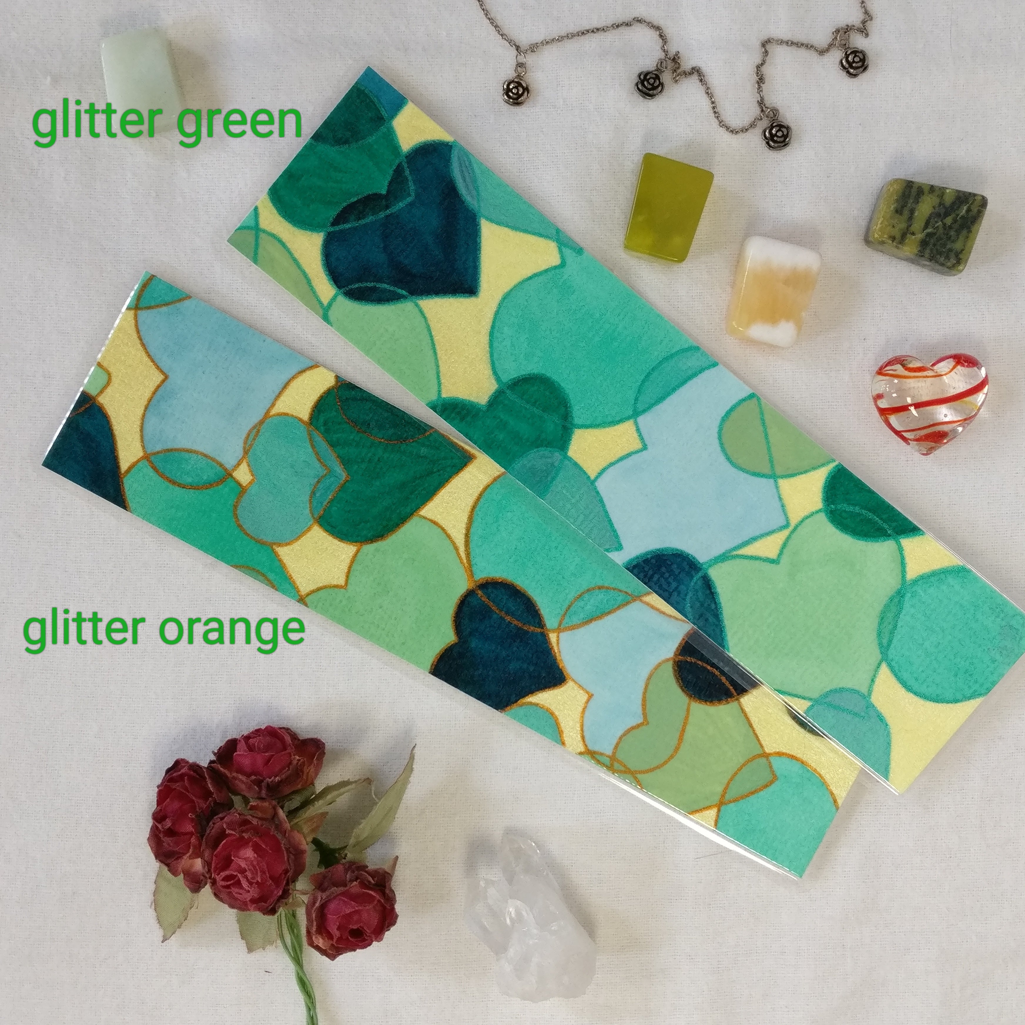 Two hand-painted watercolour hearts bookmarks in green, one with glitter orange outlines and the other one with glitter green outlines. The writing next to each bookmark makes clear which is which.