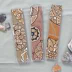 Three Mandala Bookmarks next to each other, one of each available colour. From left to right: Aqua, Purple, Orange.