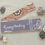 A purple Mandala Bookmark with one of the handmade package backings with a hand-written "happy reading" and a mandala corner in silver.
