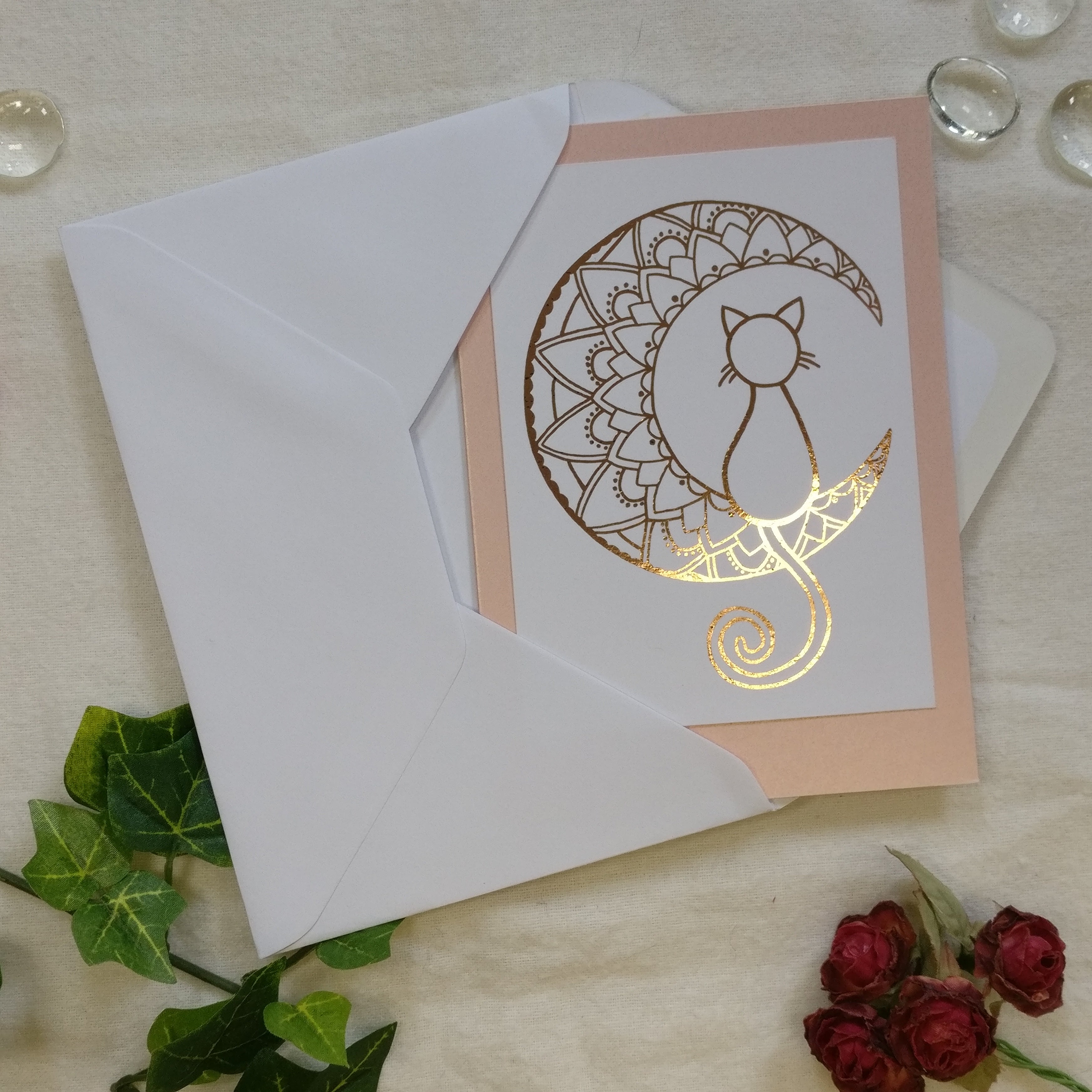 Greeting card with cat design on pearly pink cardstock, accompanied by a white envelope and decorative elements.