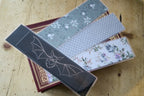 The larger Shadow Bat Bookmark with the three fabric backing options fanned out on top of a book.