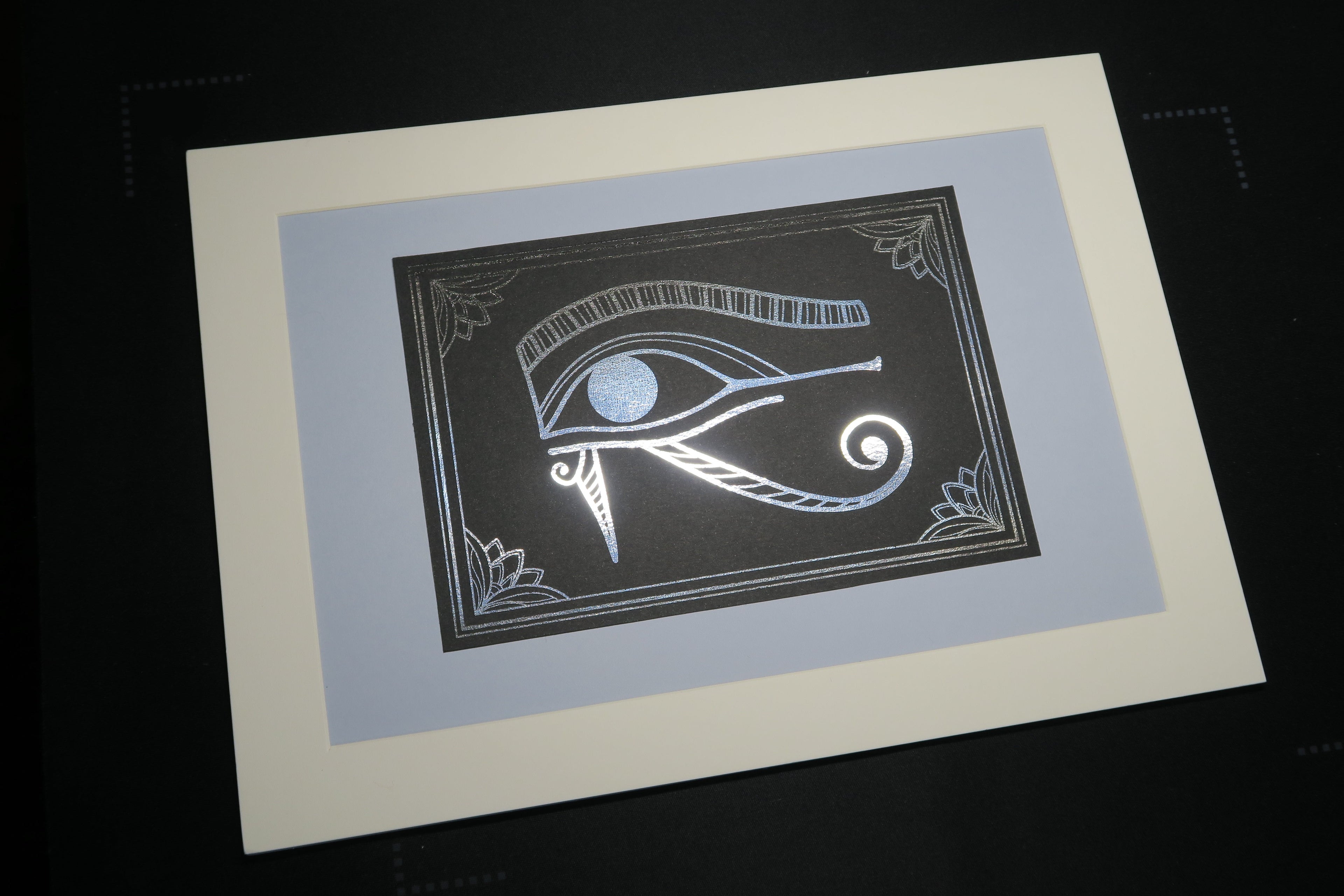 The silver foiled Eye of Horus print, mounted on a light grey backing.