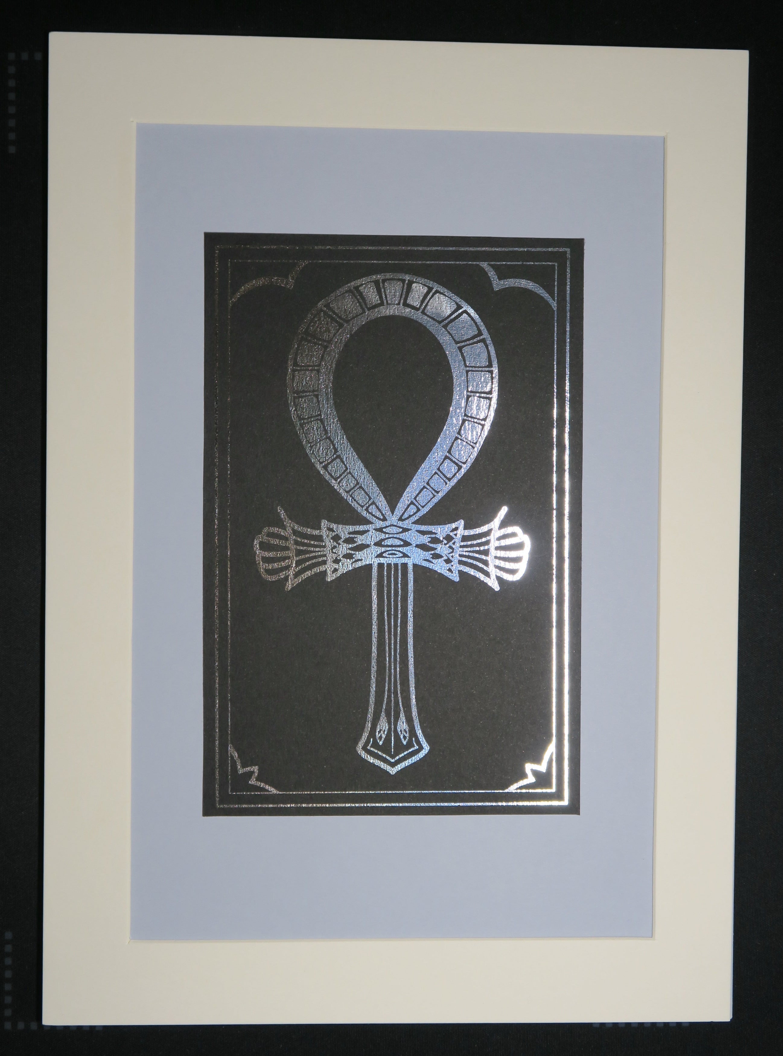 The silver foiled Ankh symbol mounted on a light grey backing.