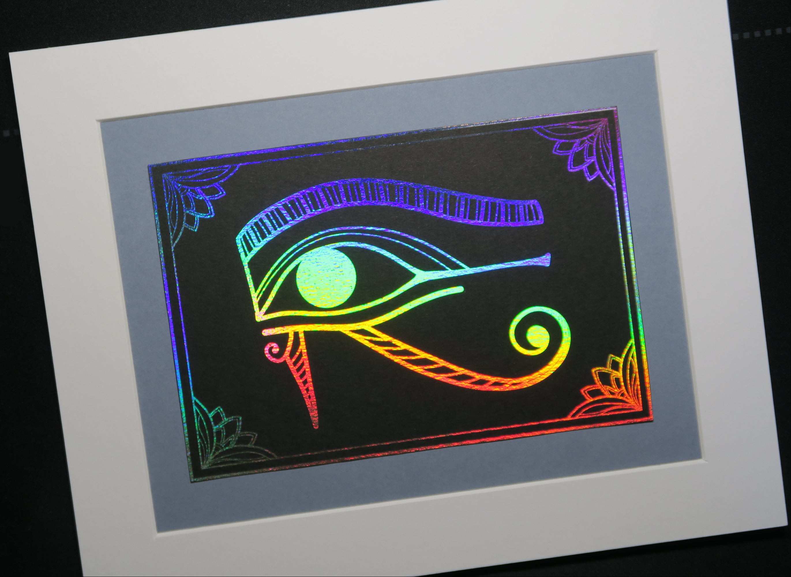 Holographic Silver foiled Eye of Horus on black cardstock, mounted on grey backing.