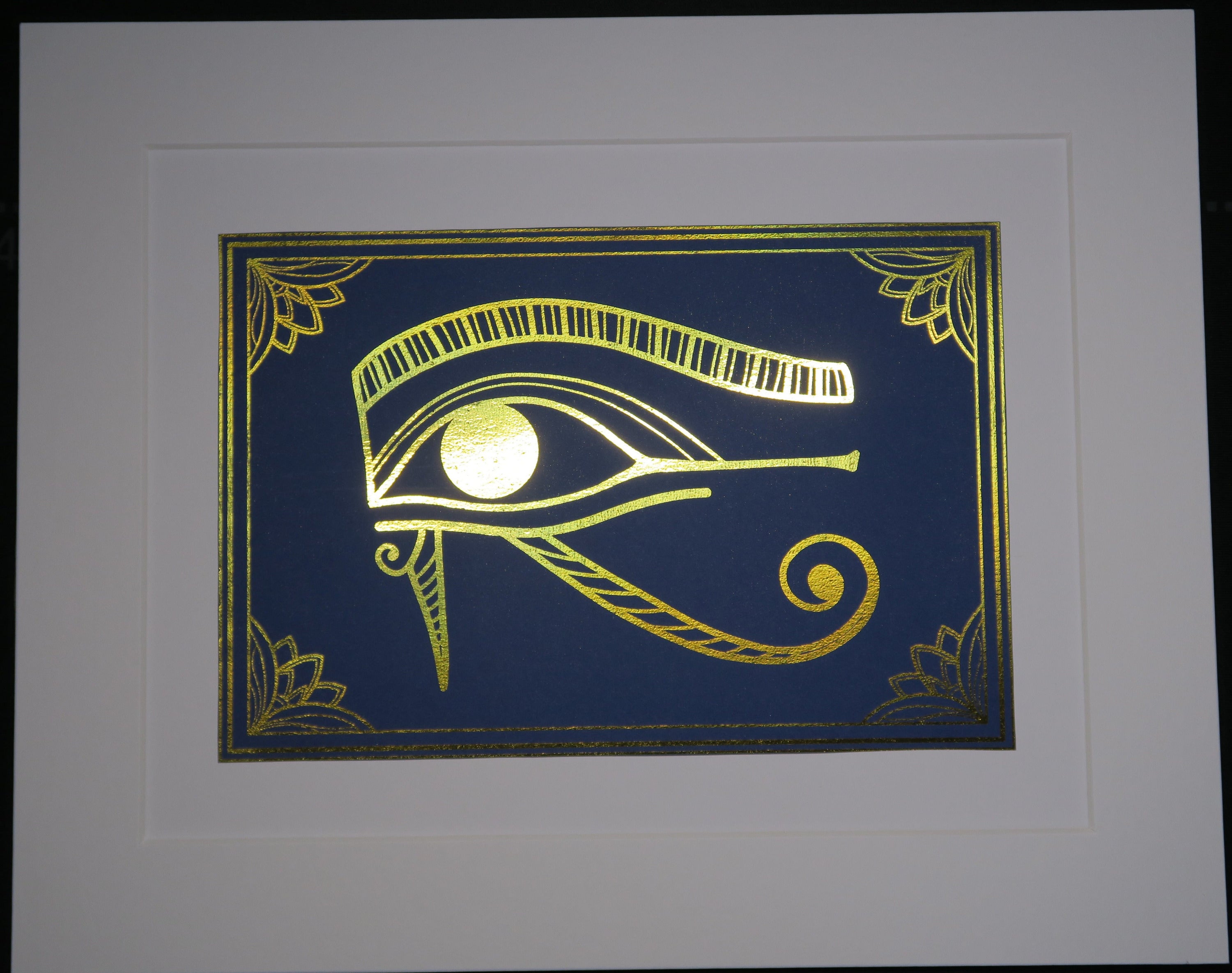 Gold foiled Eye of Horus on blue cardstock, mounted on white backing.