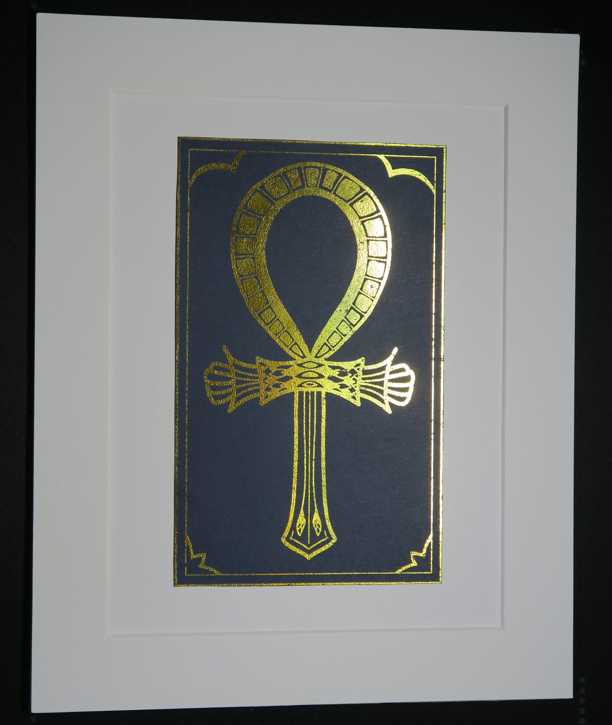 Gold foiled Ankh symbol on a navy blue card mounted on white backing.